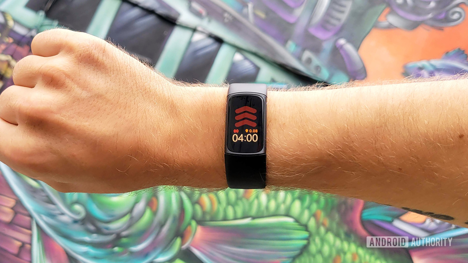 A user models the Fitbit Charge 5 in front of a painted mural wall.